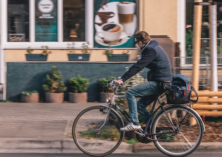 Homem de máscara andando de bicicleta. 