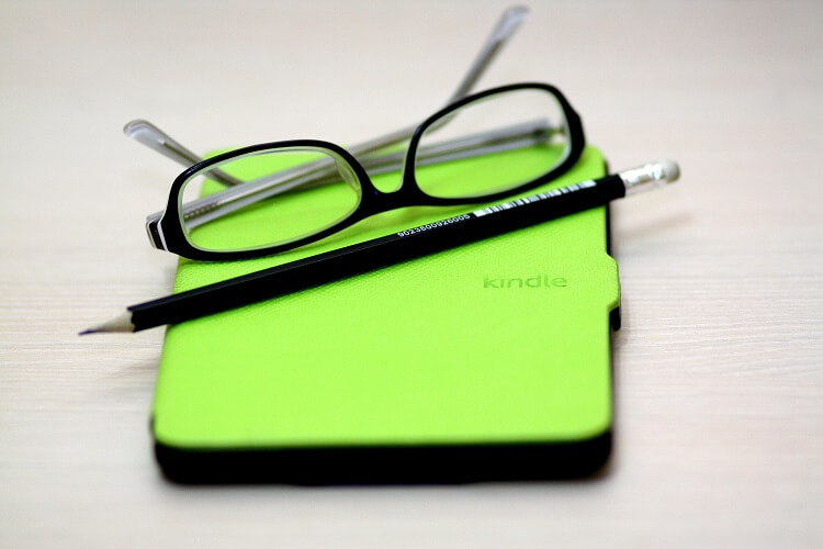 Kindle de capa verde com óculos preto em cima