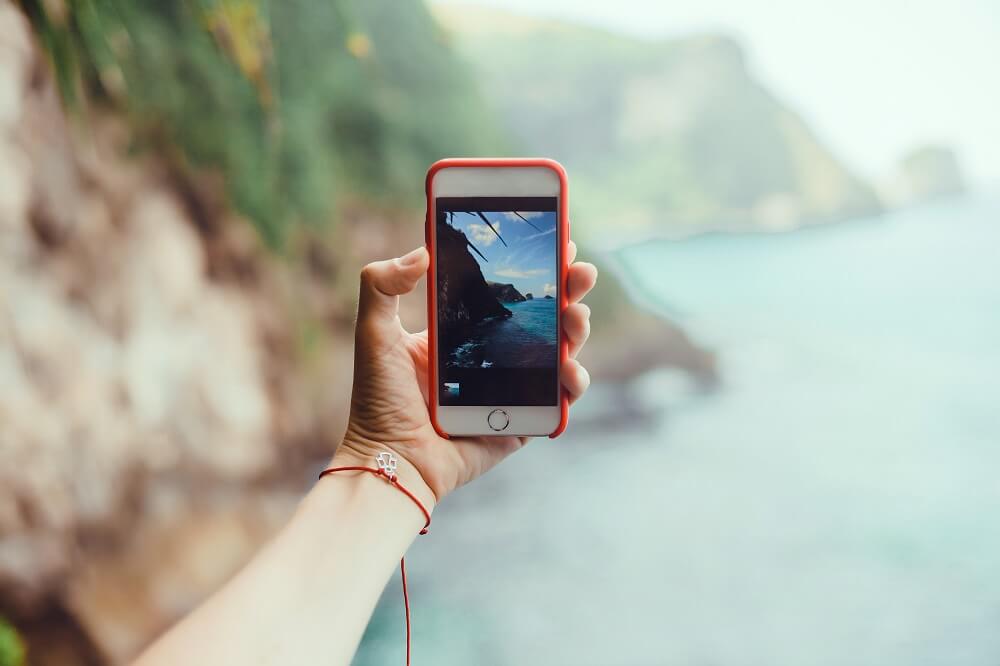 Mão segurando celular para fotografar paisagem de praia