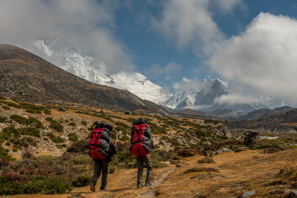 Duas pessoas em meio à montanhas, com mochilas de camping.