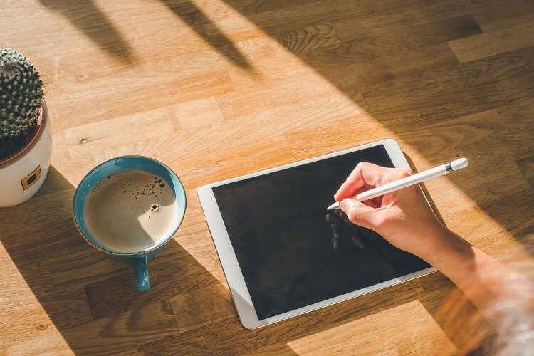 Mulher desenhando no ipad com um café do lado