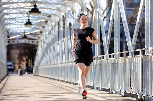 mulher correndo em uma ponte e vestindo roupas de corrida feminina, com camiseta preta e short preto