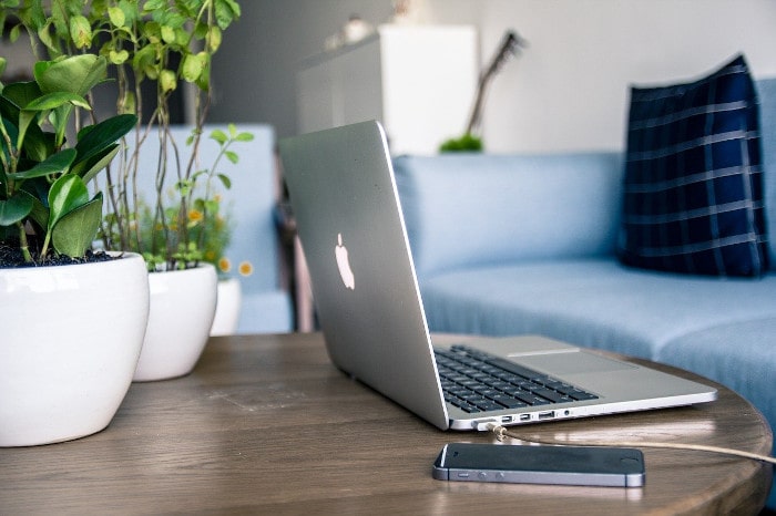 Foto de um MacBook e um iPhone sobre uma mesa, com um sofá ao lado.