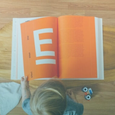 Criança lendo um grande livro com páginas laranjas.