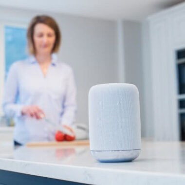Mulher utilizando um smart speaker na cozinha.