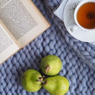 No canto esquerdo, um livro aberto, no direito, uma xícara de chá e, abaixo, três peras.