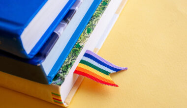 Três livros colocados um sob o outro com um marcador de páginas com as cores do arco-íris no primeiro deles.