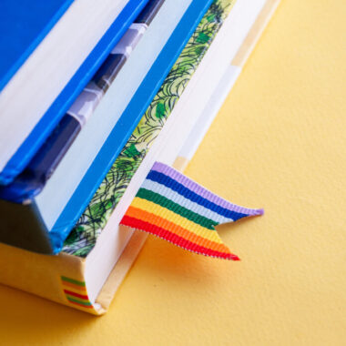 Três livros colocados um sob o outro com um marcador de páginas com as cores do arco-íris no primeiro deles.