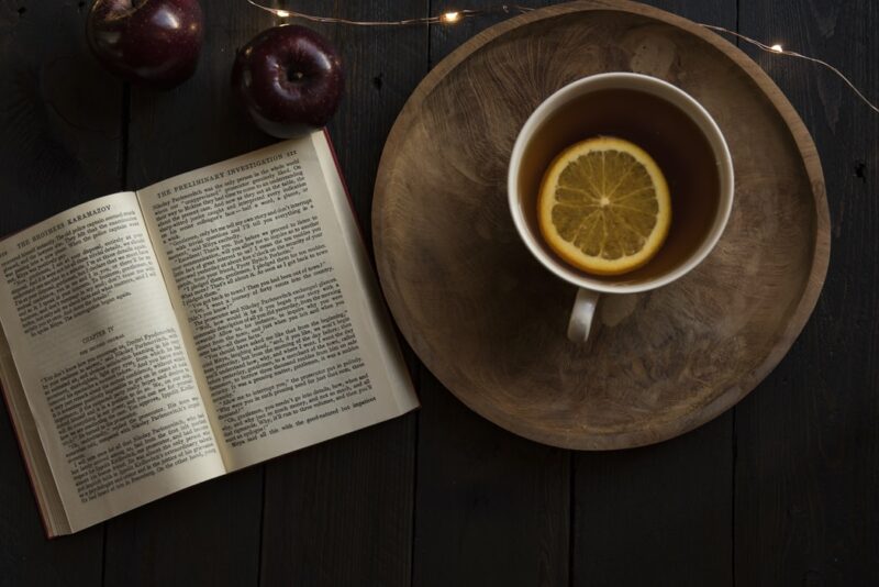 Livro aberto com xícara de chá ao lado e maçãs acima.