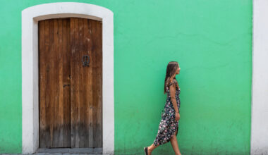 Mulher caminhando em frente de uma casa verde, enquanto veste um vestido longo de verão.