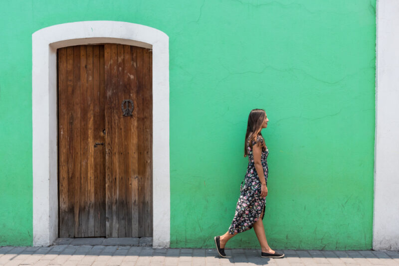 Mulher caminhando em frente de uma casa verde, enquanto veste um vestido longo de verão.