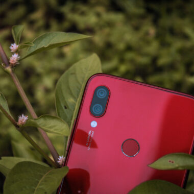 Celular Xiaomi vermelho no meio de plantas.
