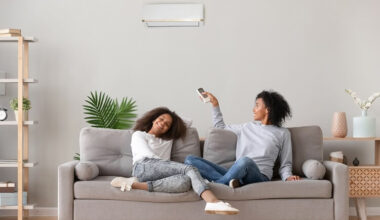 Duas mulheres negras sentadas em um sofá ligando o ar condicionado.
