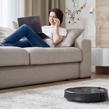 melhor robô aspirador: mulher sentada no sofá enquanto aspirador robô limpa a casa