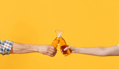 Dois braços segurando cada um uma garrafa de cerveja, em um fundo amarelo.