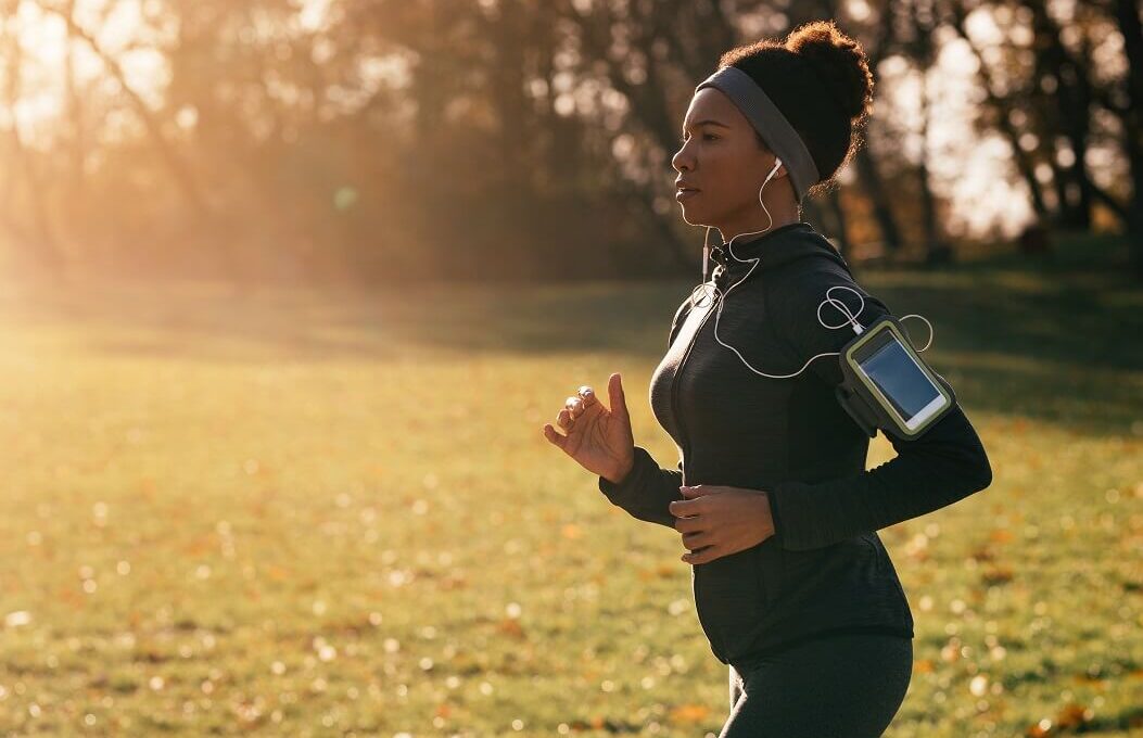 mulher correndo em um parque vestindo roupas de corrida feminina, com fone e braçadeira para celular