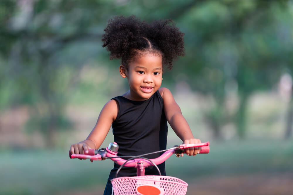 Imagem De Uma Menina Negra Em Uma Bicicleta Cor De Rosa. Ela Está Feliz.