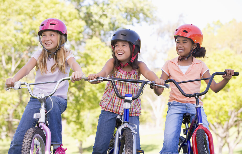 Imagem de três garotas andando de bicicleta ao ar livre.