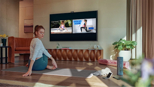 Imagem de uma mulher se exercitando na sala da casa, enquanto assiste a um vídeo na TV Quadro da Samsung.