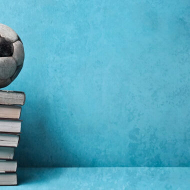 Livros sobre futebol - bola de futebol sobre uma pilha de livros, num fundo azul.