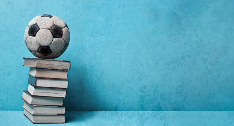 Livros sobre futebol - bola de futebol sobre uma pilha de livros, num fundo azul.