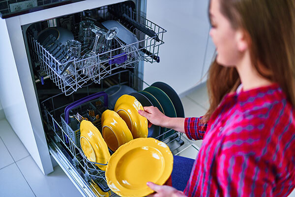 mulher colocando pratos amarelos na lava-louças.