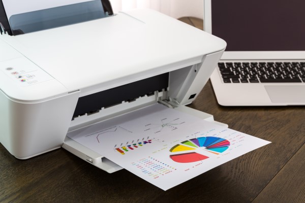 Impressora multifuncional branca imprimindo páginas coloridas.