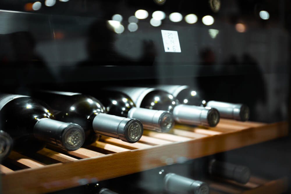 Imagem de cinco garrafas de vinho tinto dentro de uma adega climatizada.