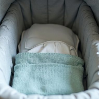 Moisés de carrinho de bebê cinza com manta verde-azulada dobrada, visto de cima